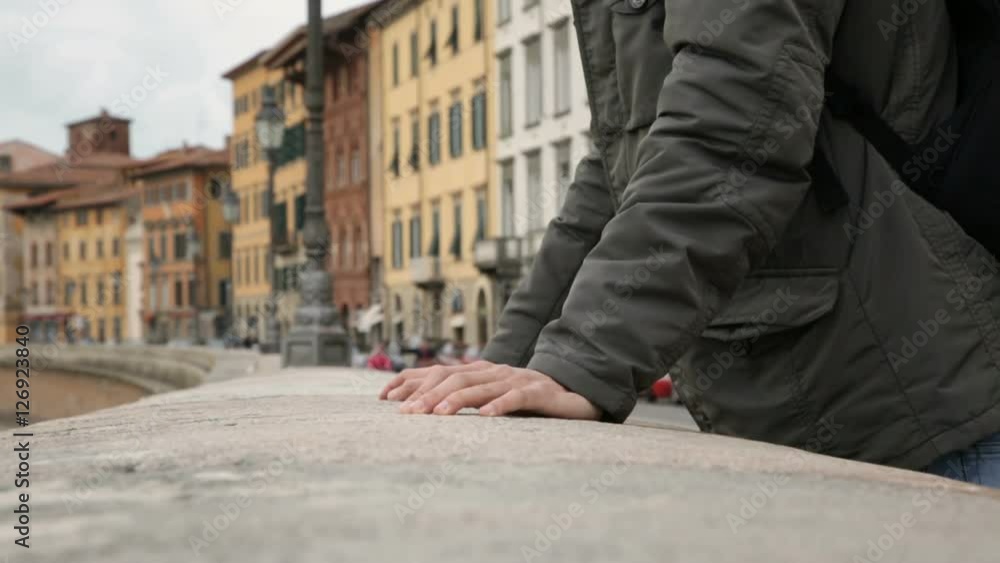 Hand of a man lean against the river bank in a city with colored houses as background. Hand of a man lean against the river bank in a city with colored houses as background.