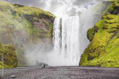 Two people lokking at spectacular Scogafoss waterfall in Iceland