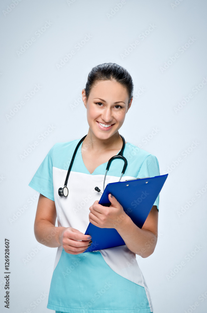 Young woman doctor in scrubs with a black pediatric stethoscope holding blue tablet for papers. Young woman doctor in scrubs with a black pediatric stethoscope holding blue tablet for papers.