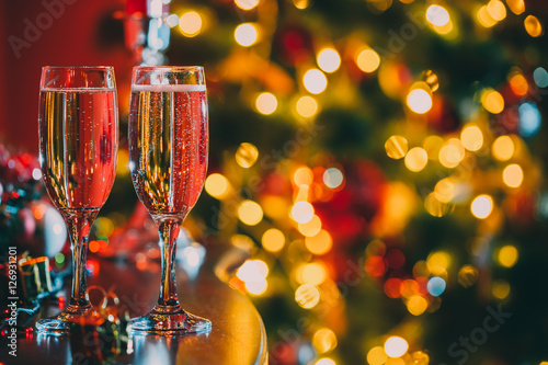 Beautiful two glasses of champagne standing on the table in the background of a blurred room with a decorated Christmas tree and fireplace. Soft focus. Shallow DOF