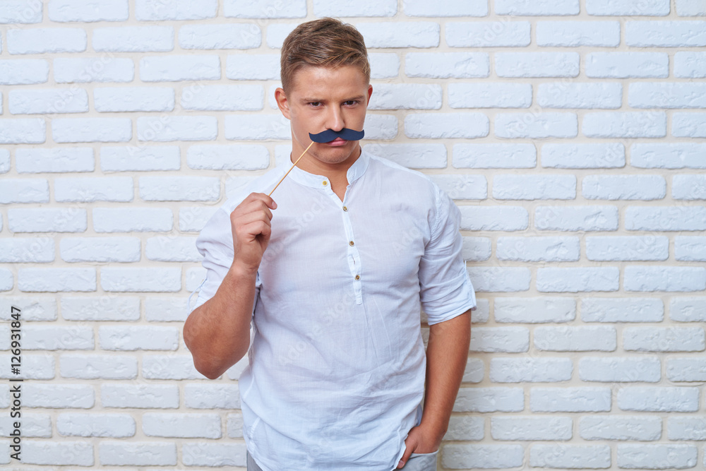 Handsome boy frowning when wearing black paper moustache on stic Handsome boy frowning when wearing black paper moustache on stic