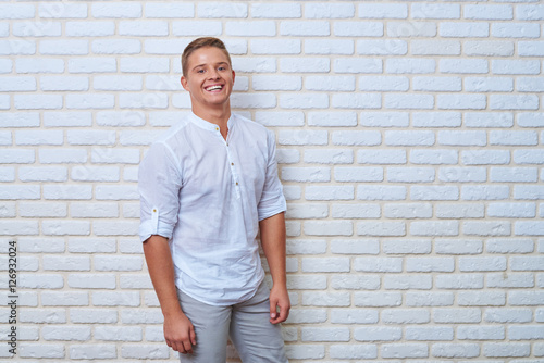 Portrait of exhilarated young man against brick wall with fashio
