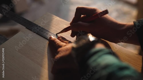 hand of a carpenter taking measurement of a wooden plank. sun flare ob background