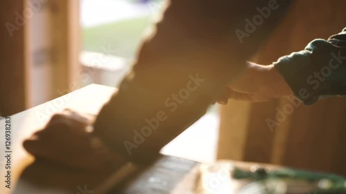 hand of a carpenter taking measurement of a wooden plank. sun flare ob background