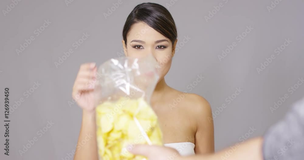 Happy woman grabbing potato chips from a plastic bag with a look of gleeful anticipation Happy woman grabbing potato chips from a plastic bag with a look of gleeful anticipation