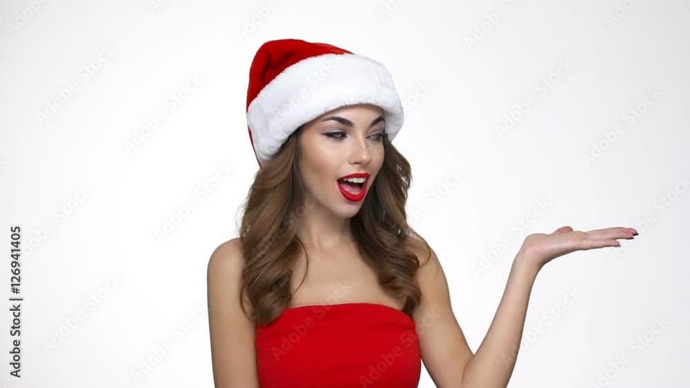 Smiling playful young woman in red santa claus costume holding copyspace on palms Smiling playful young woman in red santa claus costume holding copyspace on palms