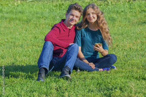 Couple teenagers sitting on the green lawn with a smartphone