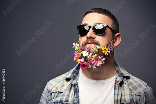 Handsome man in sunglasses with beard of flowers on dark background