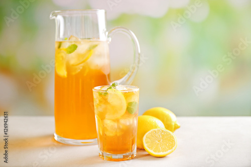 Glass and jug of iced tea with lemon slices on table