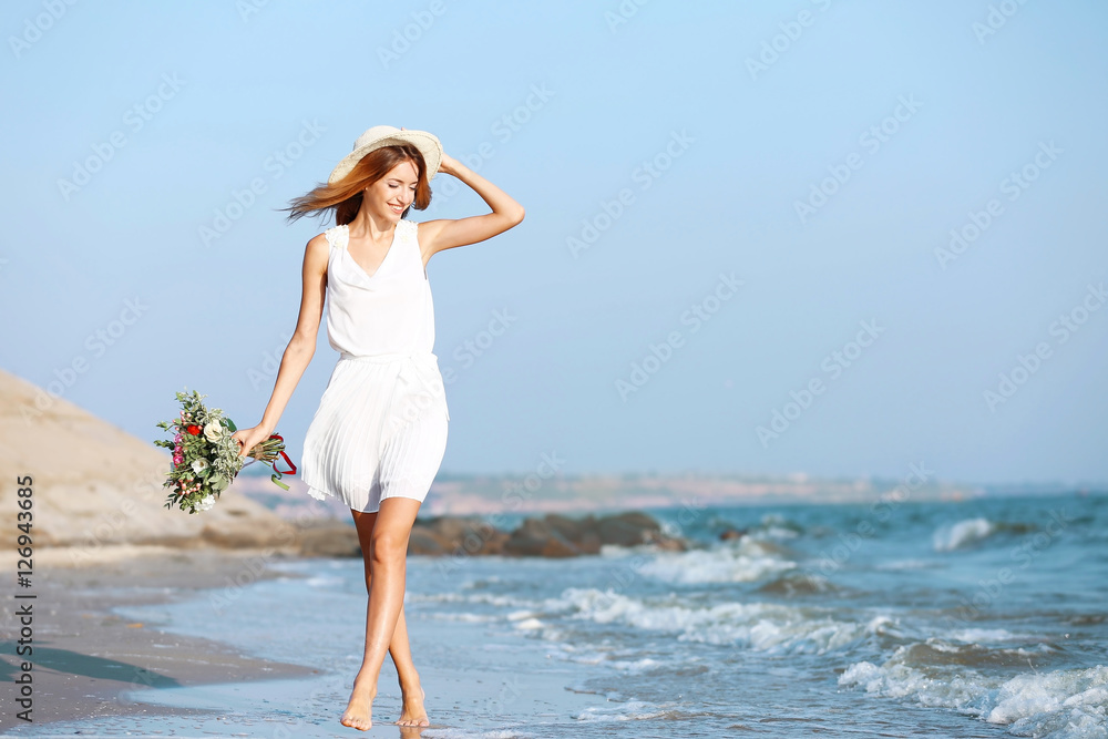 Young happy woman with bouquet of flowers walking along seashore