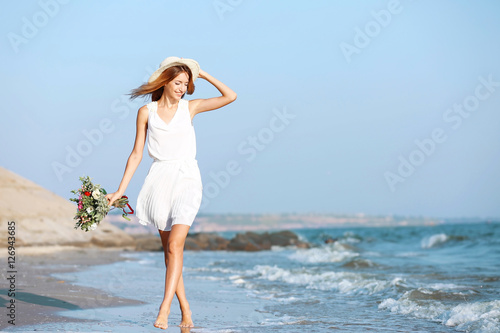 Young happy woman with bouquet of flowers walking along seashore