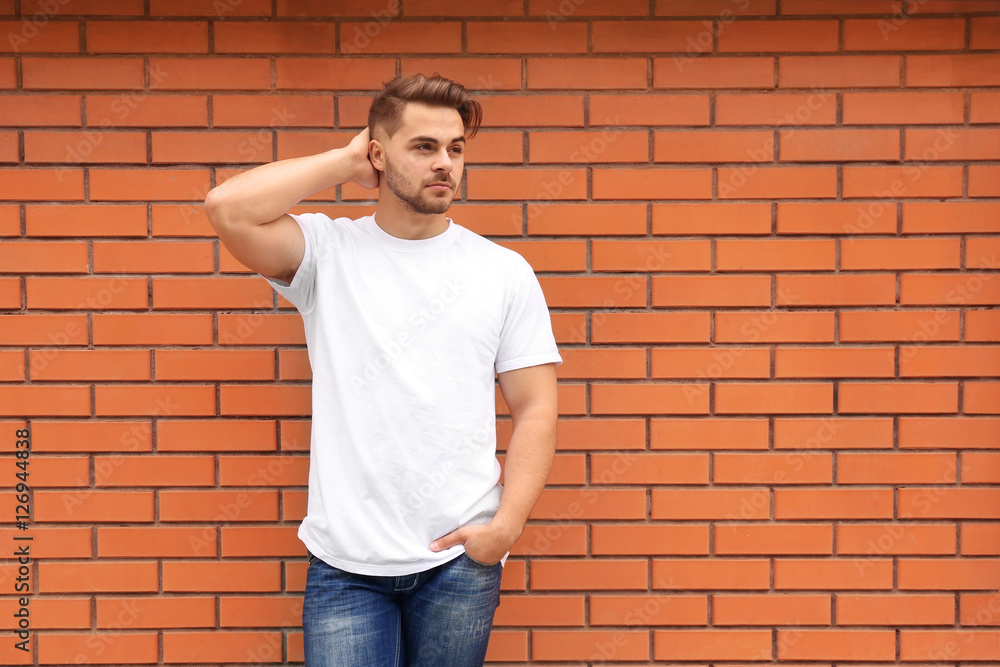 Young man in blank t-shirt standing against brick wall Young man in blank t-shirt standing against brick wall