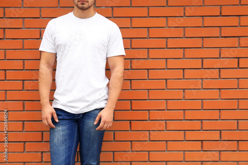 Young man in blank t-shirt standing against brick wall, closeup
