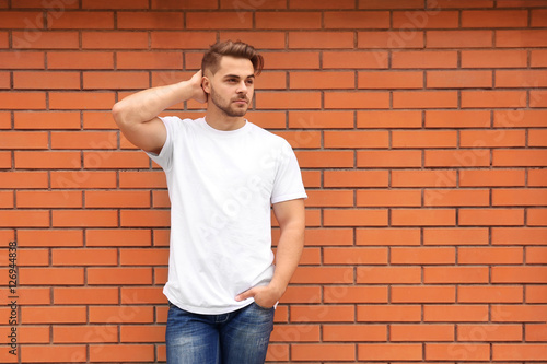 Young man in blank t-shirt standing against brick wall