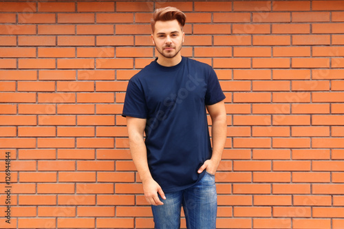 Young man in blank t-shirt standing against brick wall