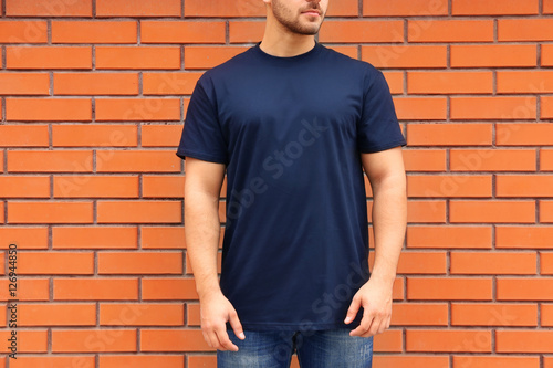 Young man in blank t-shirt standing against brick wall, closeup