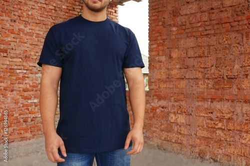 Young man in blank t-shirt standing near brick wall, closeup © Africa Studio