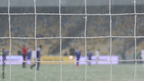 View of goal net during snowfalls. Blurred football players on background