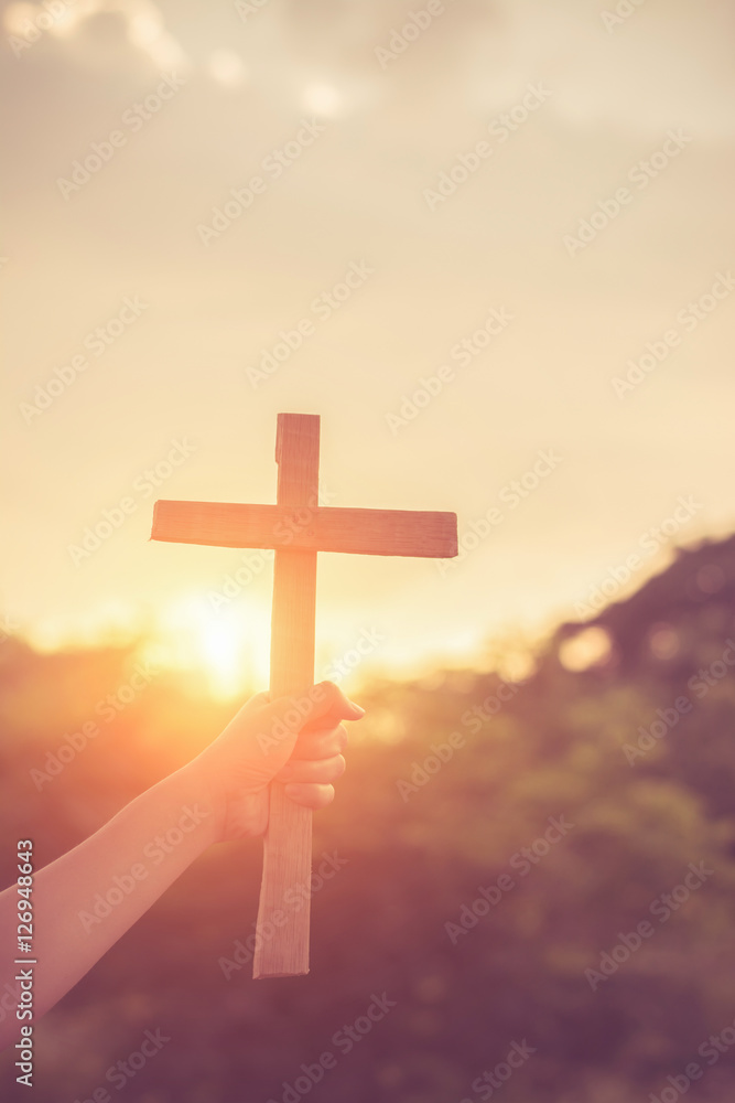 Close up woman hand holding wood cross or religion symbol shape over a sunset sky with clouds background for God,Christianity, religious, faith, holy, spiritual, Jesus, belief or resurrection.