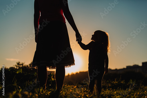 silhouette of mother and daughter holding hands at sunset