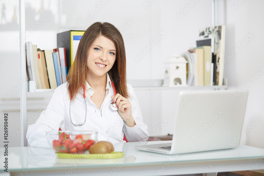 Smiling nutritionist writing medical records with fresh fruit on foreground
