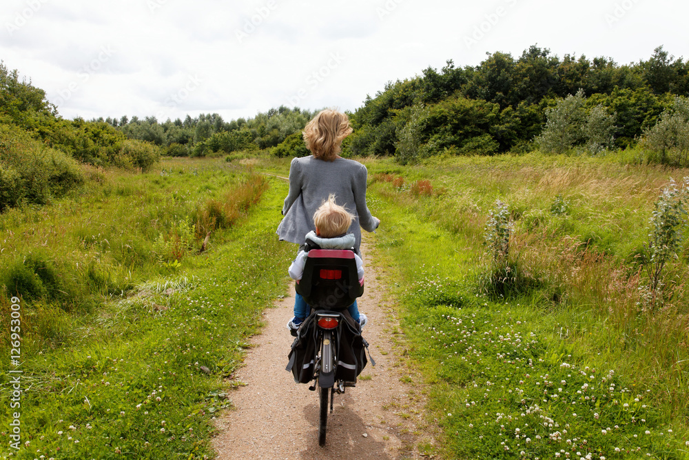 woman with child cycling away in nature in summer woman with child cycling away in nature in summer