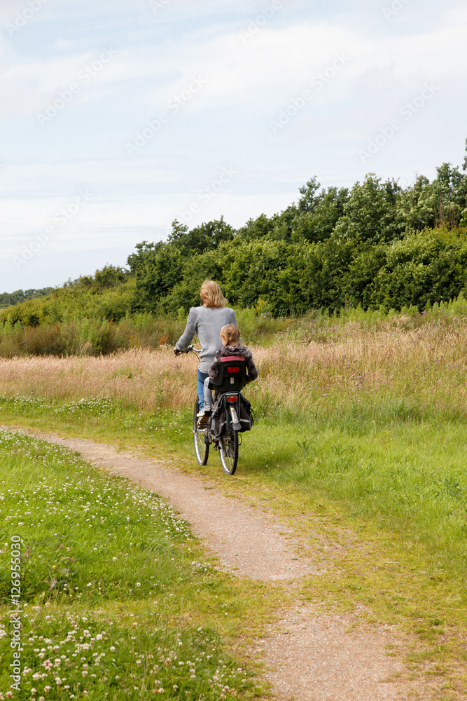 Woman with child behind cycling away in beautiful nature