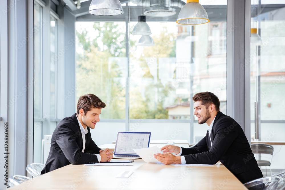 Two happy businessmen working together using laptop on business meeting
