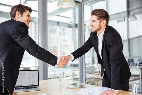 Two cheerful businessmen shaking hands on business meeting