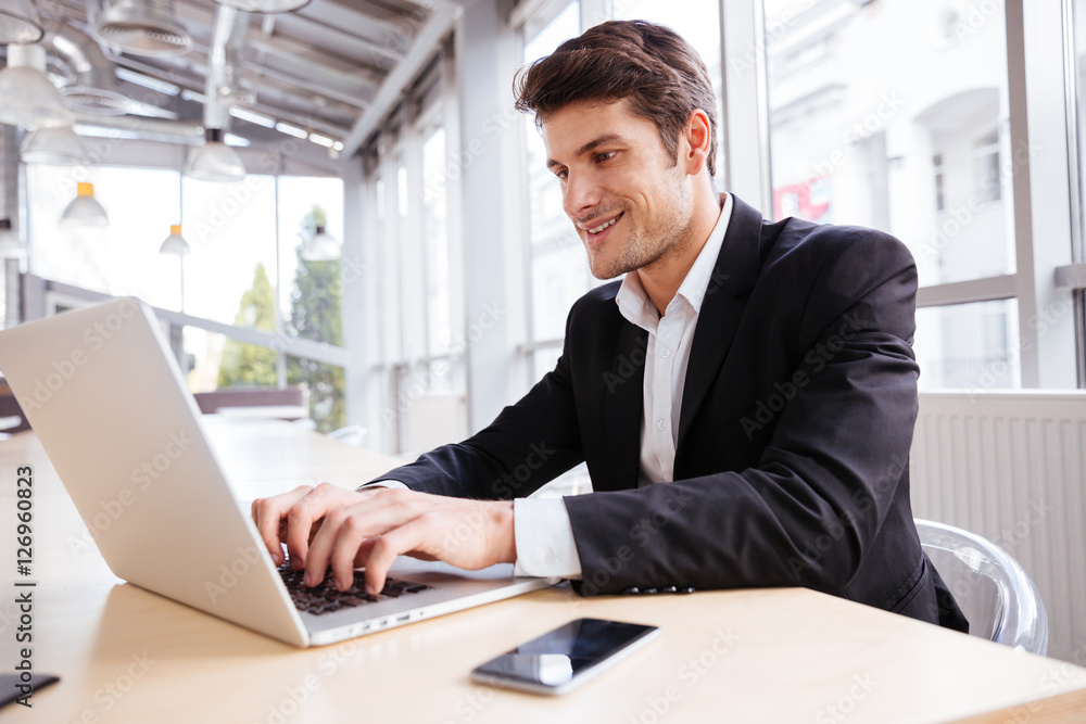 Cheerful businessman using laptop and mobile phone at the table Cheerful businessman using laptop and mobile phone at the table