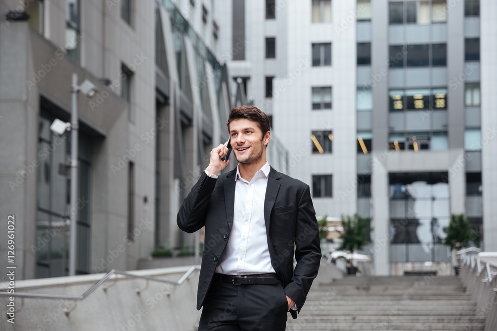 Cheerful young businessman walking and talking on cell phone