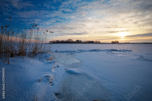 Beautiful winter landscape with frozen lake and sunset sky. 