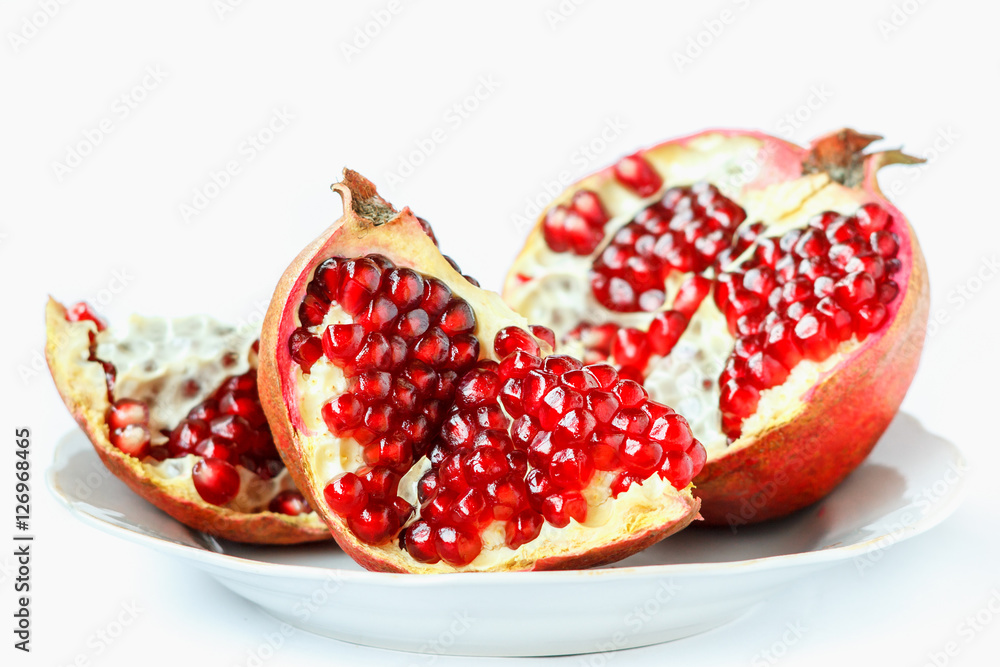 Ripe juicy pomegranate fruit (Punica granatum) in a white plate isolated on white background Ripe juicy pomegranate fruit (Punica granatum) in a white plate isolated on white background