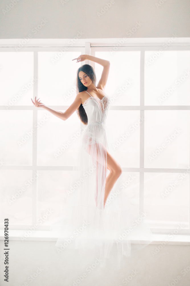 Luxury sexy girl, she is dancing on window sill in white light.