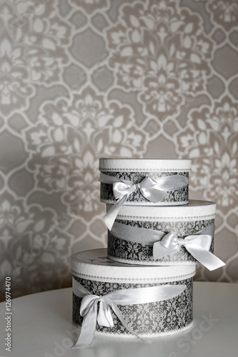 Three round celebration gift boxes with silver ribbon bows on white table. Stack of presents in luxury interior.
