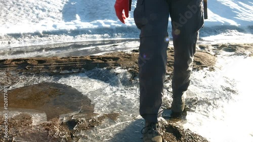 A hiker steps over some thin ice near a glacier in Etha, Greenland photo