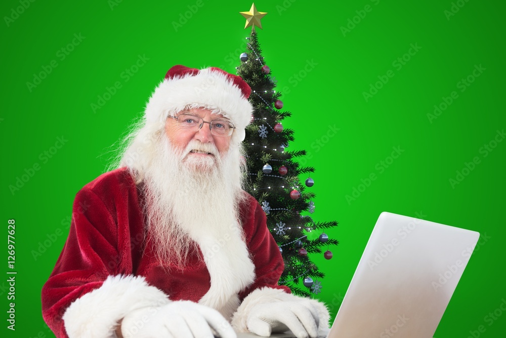 Naklejka premium Santa claus using laptop against green background