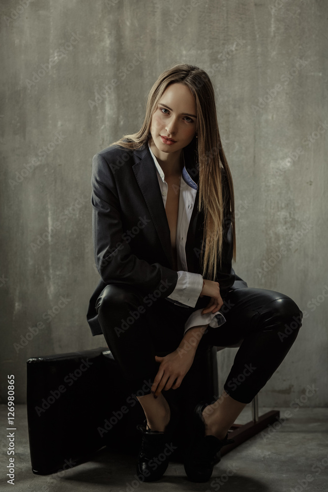 The girl in classic jacket, blouse and leather pants sits on a b
