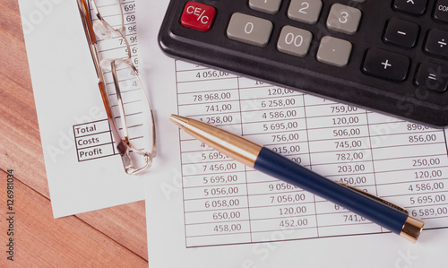 Pen, glasses and calculator on paper tables with numbers