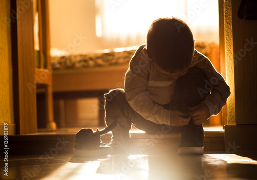 Foto Little boy on doorstep trying to put his shoes on. Natural light.