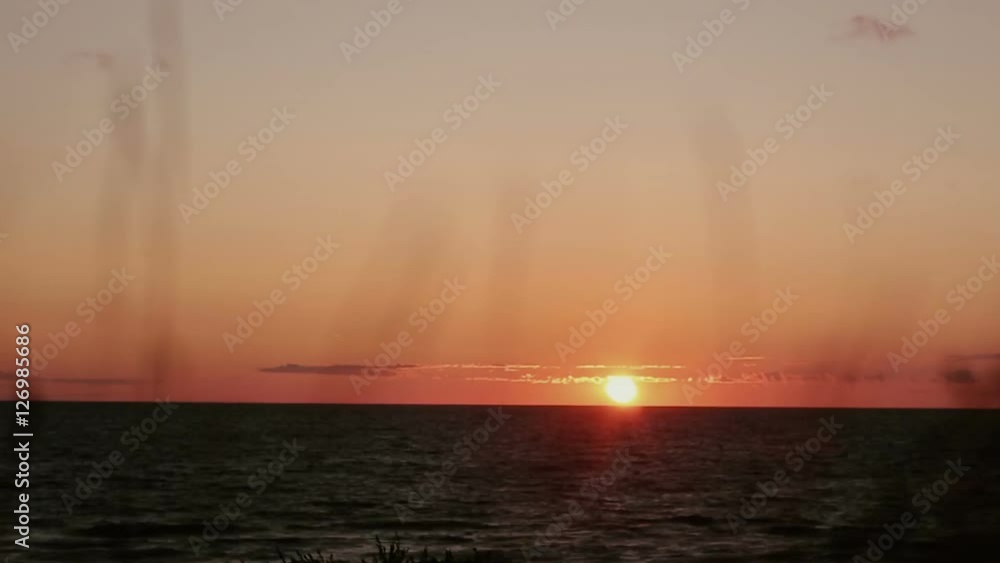 A time lapse video of pinky-orange sunset at sea side with dry grass swaying in the front view. A time lapse video of pinky-orange sunset at sea side with dry grass swaying in the front view.