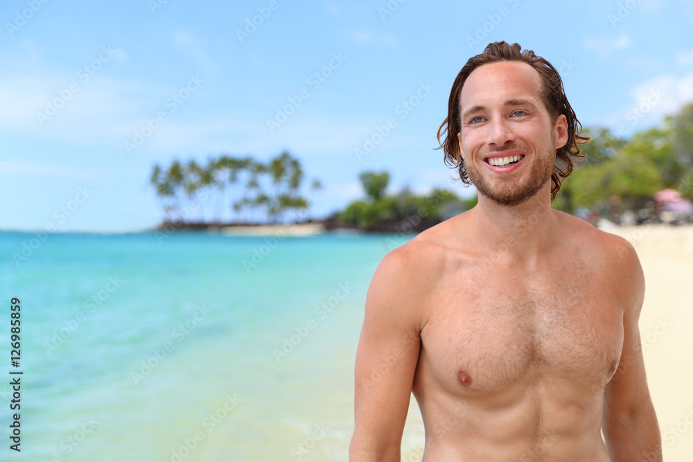 Handsome young man smiling looking at turquoise ocean on summer beach vacation. Portrait of an attractive caucasian male model with sexy abs relaxing on a tropical travel destination. Handsome young man smiling looking at turquoise ocean on summer beach vacation. Portrait of an attractive caucasian male model with sexy abs relaxing on a tropical travel destination.