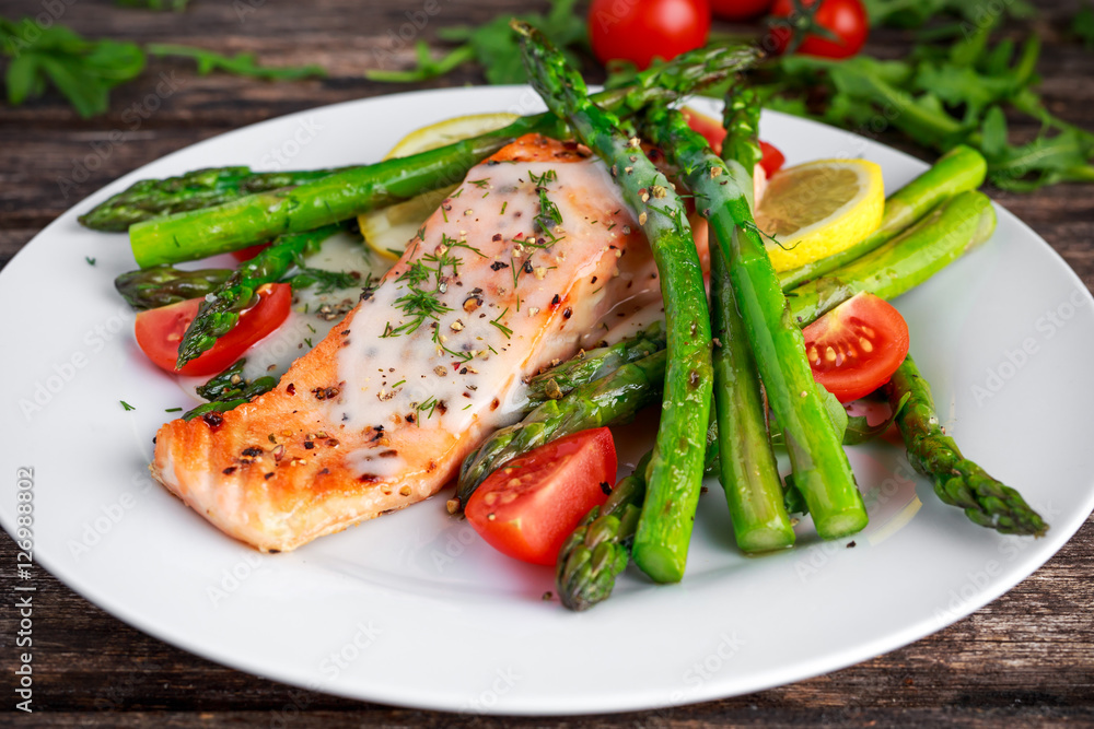 Fried salmon with asparagus, tomatoes, lemon, yellow lime on white plate Fried salmon with asparagus, tomatoes, lemon, yellow lime on white plate