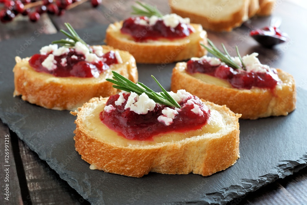 Holiday crostini appetizers with cranberry sauce, brie, feta and rosemary on a slate server Holiday crostini appetizers with cranberry sauce, brie, feta and rosemary on a slate server