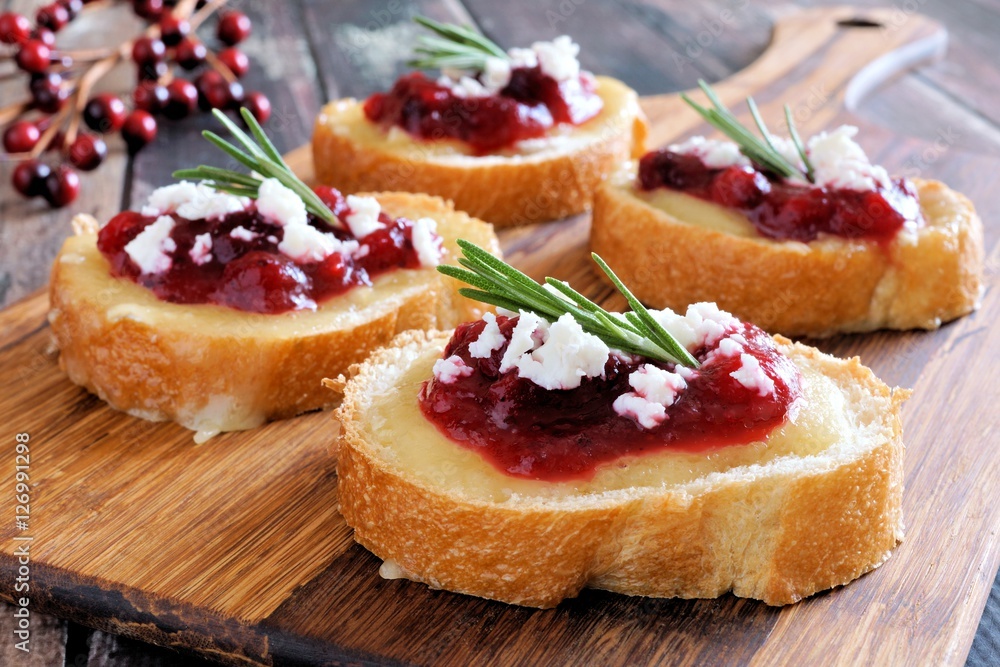 Holiday crostini appetizers with cranberry sauce, brie, feta and rosemary on a wooden server
