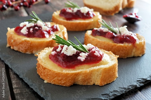 Holiday crostini appetizers with cranberry sauce, brie, feta and rosemary on a slate server