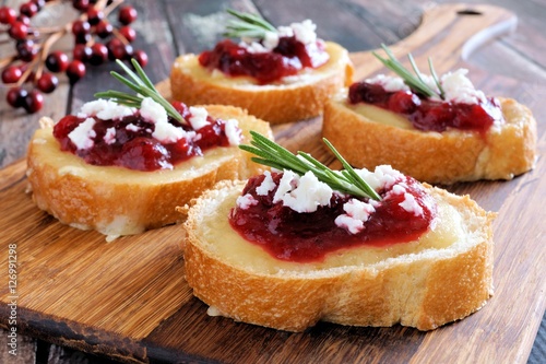 Holiday crostini appetizers with cranberry sauce, brie, feta and rosemary on a wooden server