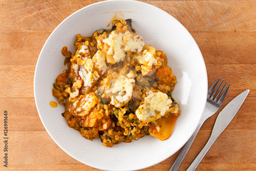 Overhead view of a lentil and vegetable hotpot with a cheesy potato topping in a white china bowl