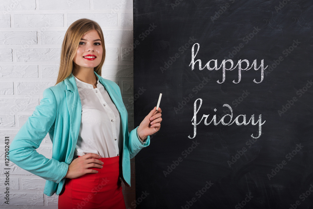 An attractive young woman with chalk at the blackboard with text happy friday An attractive young woman with chalk at the blackboard with text happy friday