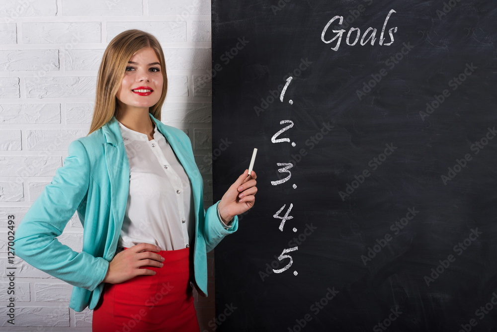 An attractive young woman with chalk at the blackboard with text goals An attractive young woman with chalk at the blackboard with text goals